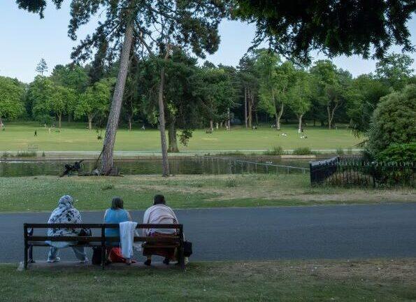 Three women sat on a bench looking out at the lake at Cannon Hill Park
