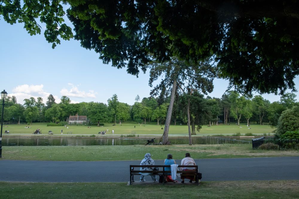 Three women sat on a bench looking out at the lake at Cannon Hill Park