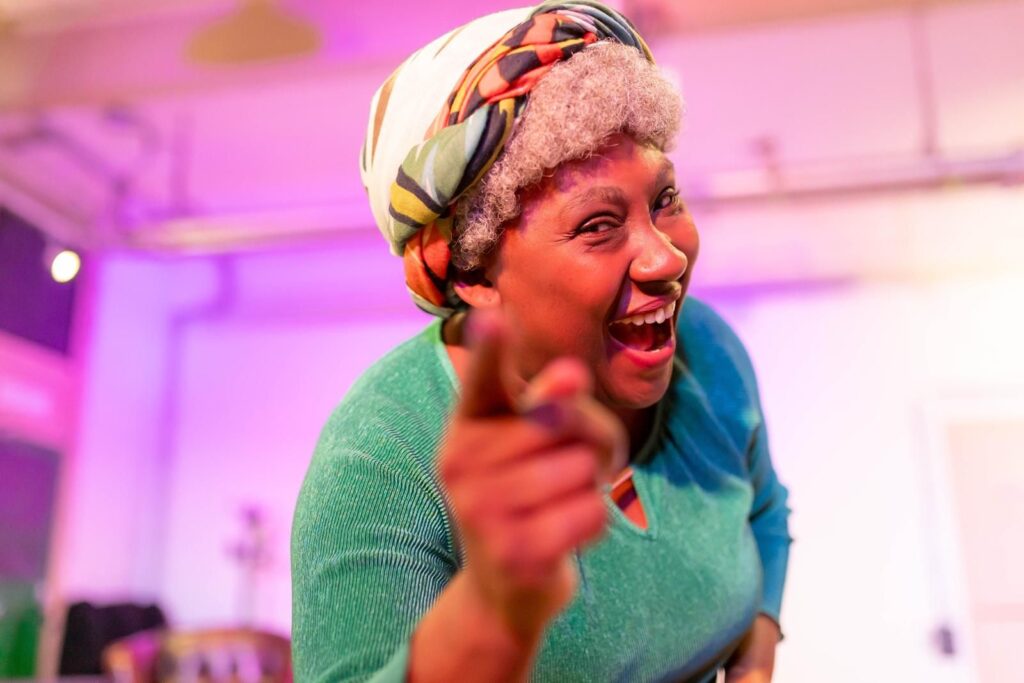 An elderly black woman smiling and pointing at the camera