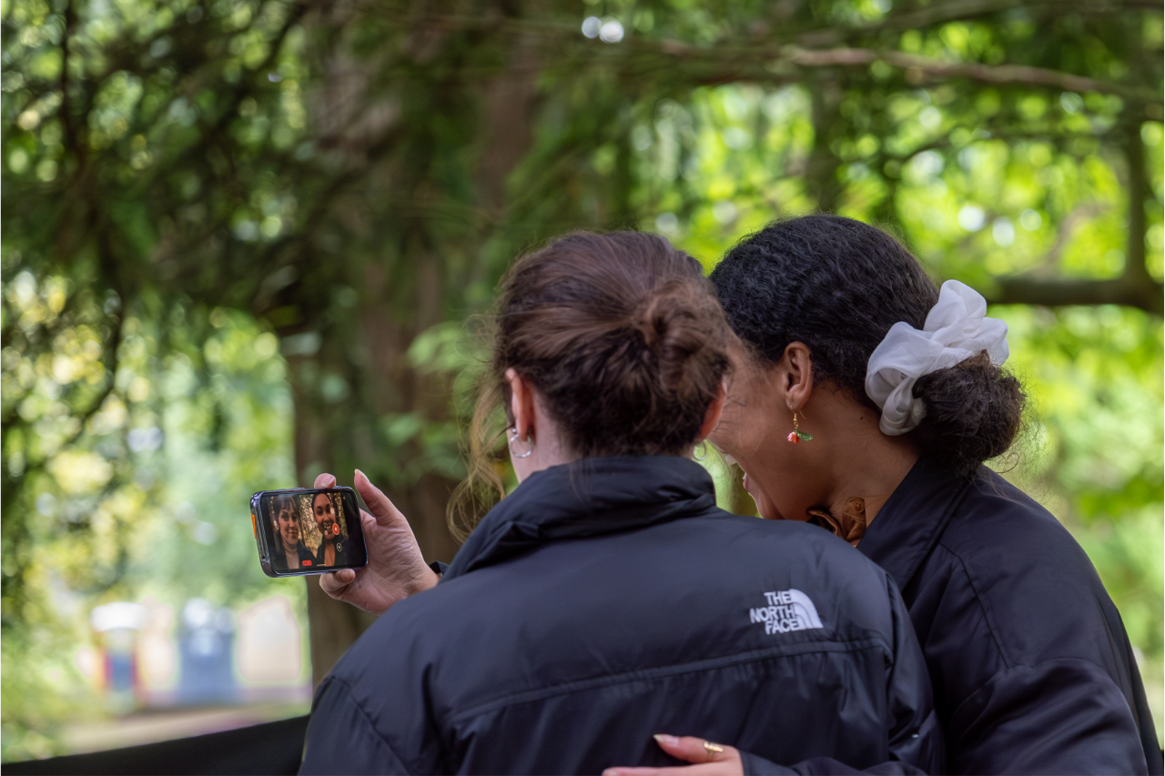 Two women in a woods with their backs to the camera taking a selfie 